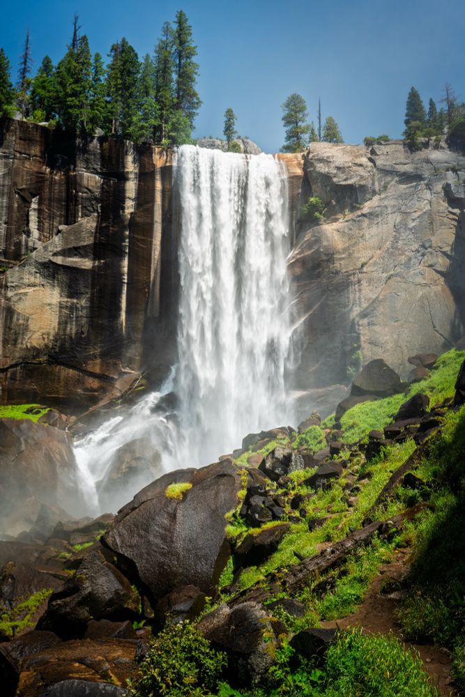 A majestic waterfall descending to a rocky valley under bluebird skies