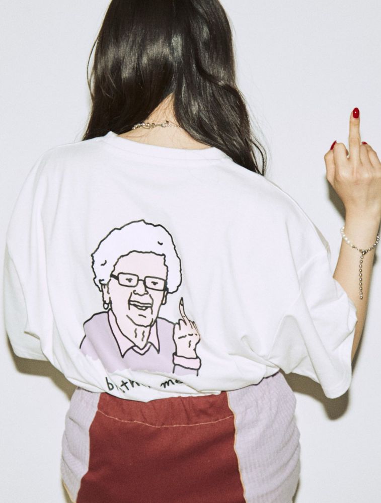 BrotherMerle 半袖Tシャツ着画　後ろ身頃に中指を立てた人物(上品な服装で眼鏡をかけた年配の女性表象)のイラストがプリントされている　こちらに背中を向けたモデルもイラストに合わせて右手の中指を立てている