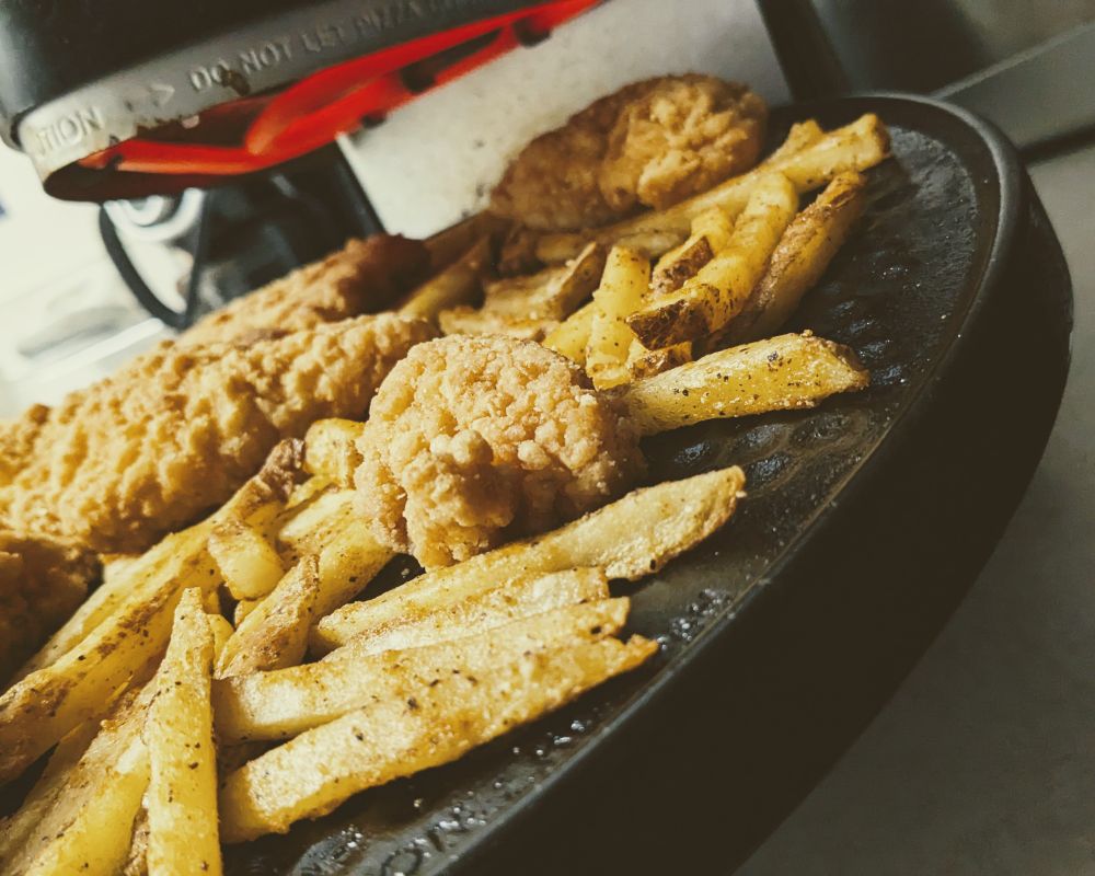 chicken strips and seasoned fries cooking on an open rotisserie oven 