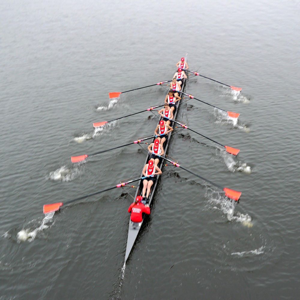 Eight rowers in a long boat on water, synchronized and paddling with red oars.