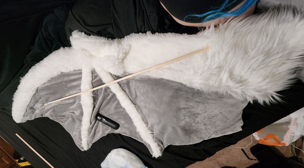 Work in progress, white, bat, fursuit arm wing with a long dowel over it as well as a Roku remote in the left-center