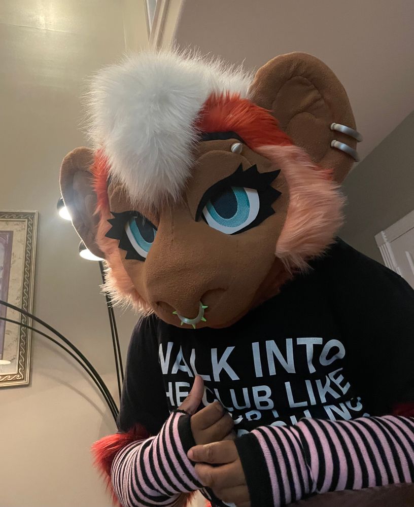 Antyres the red monkey fursuiter slightly leaning over the camera wearing a black shirt and elbow length knitted fingerless gloves 