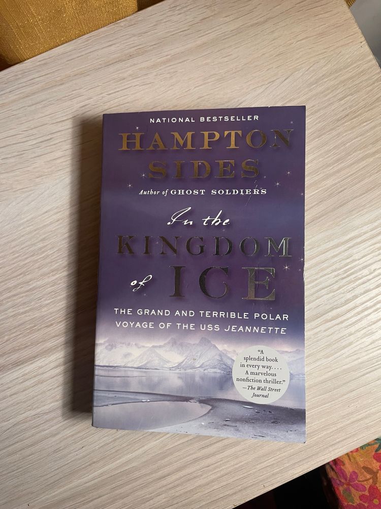 In the Kingdom of Ice by Hampton Sides rests on a wooden surface. The cover features and illustration of an Arctic landscape.