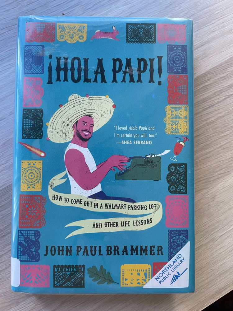 ¡Hola Papi! by John Paul Brammer rests okay a wooden shelf. 