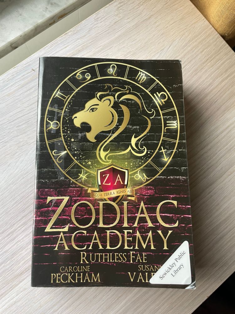 Ruthless Fae by Caroline Peckham and Susanne Valenti rests on a wooden surface. 