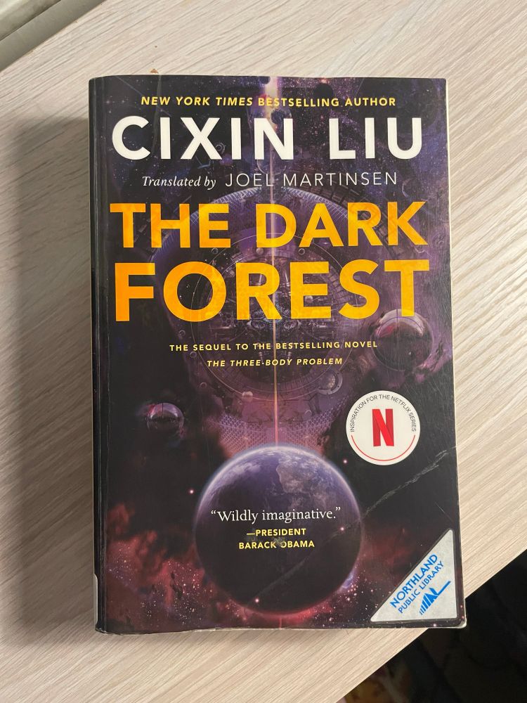The Dark Forest by Cixin Liu rests on top of a wooden shelf. 