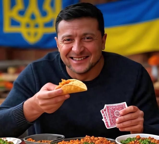AI'd meme (99%sure) of Zelensky at table loaded with taco fixings. TACO in one hand, hand of red playing cards in the other. He's in his classic navy blue long sleeve top. Big smile. Blue and Yellow Ukraine flags behind him. 