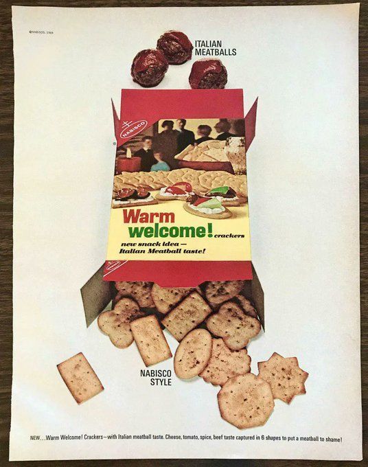 An ad for Warm Welcome! crackers. There is a red box with the image of a party/appetizer table with a spread of crackers and toppings, and guests in the background. The top of the box is open, and sauce-covered meatballs are entering it. The bottom of the box is open, and a cascade of geometric shape crackers spill out. The ad copy reads that this product is "Italian meatballs...Nabisco style."
