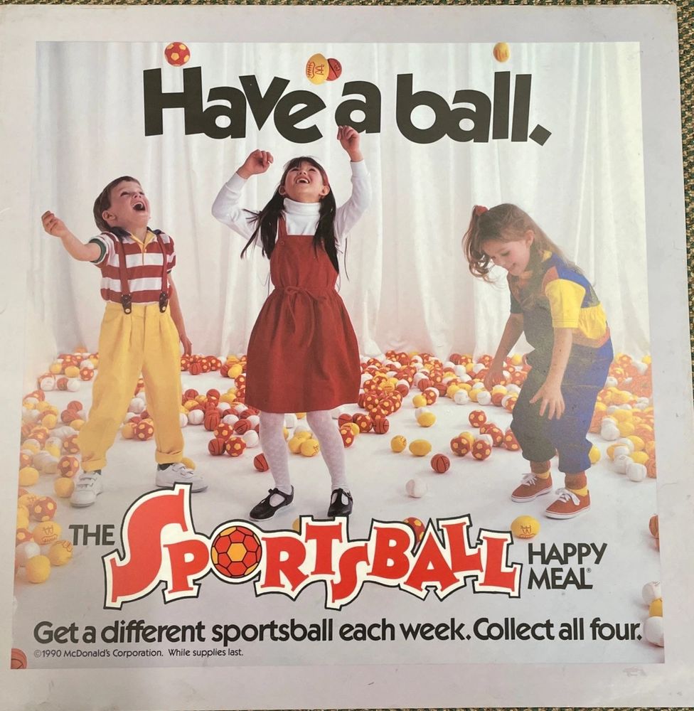 An ad for McDonald's "Sportsball" Happy Meal, with a picture of 3 little kids joyously playing with colorful soccer balls, basketballs, and baseballs in a white room