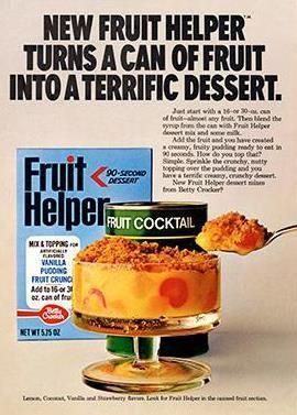 An ad for Fruit Helper, featuring a clear trifle dish filled with fruit cocktail and a crumb topping, next to a spoon holding fruit and crumb topping, and a can of fruit cocktail 