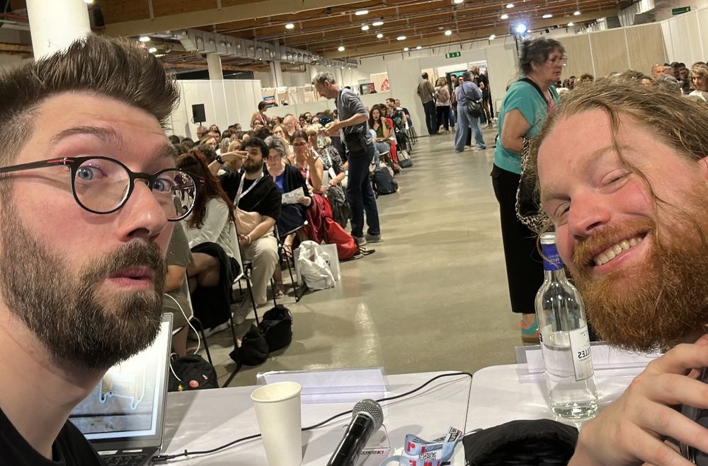 Nos deux têtes de glandus devant l’assistance de la table ronde à laquelle on a participé au congrès. En arrière plan un bibliothécaire inspiré photobomb avec le signe universel des deux doigts coupe-faim. 