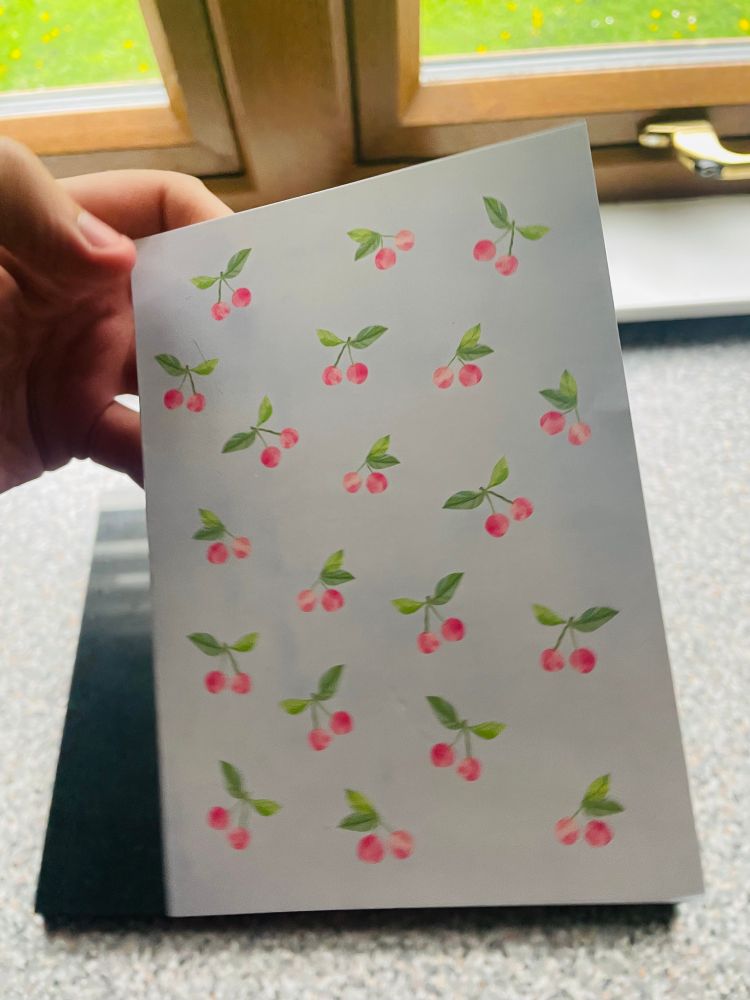 Front cover of a card with lots of red/pink cherries, with stems and greens leaves.