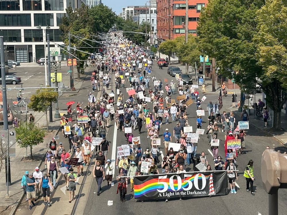 A crowd of people marching down the street in Portland, Oregon. A banner at the front of the march says, 