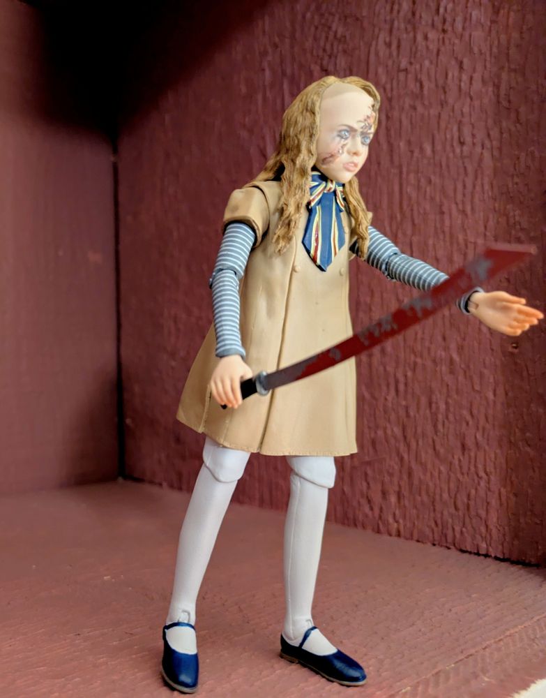 M3GAN figurine based on the first movie. She has an outstretched left hand and a bloody paper guillotine (from a paper cutter machine) in the other 