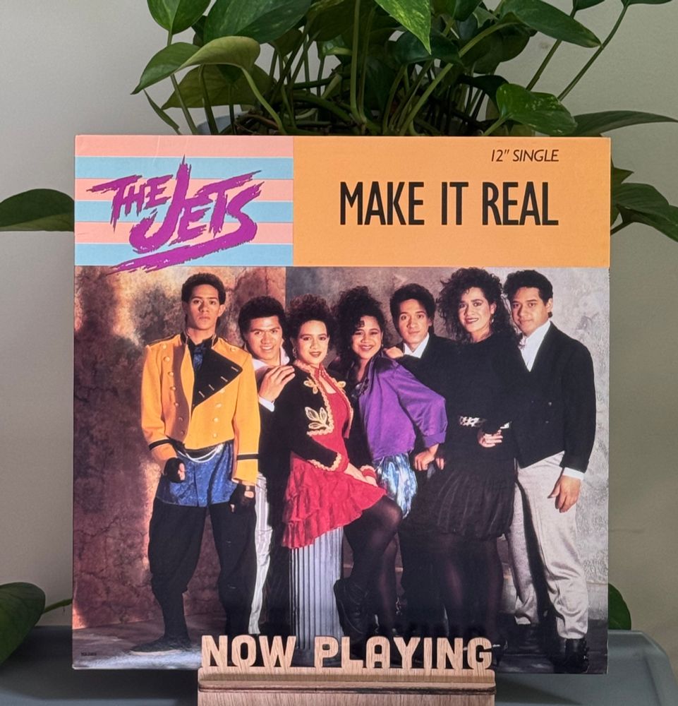 A record album in a stand on a table with a plant behind it. 