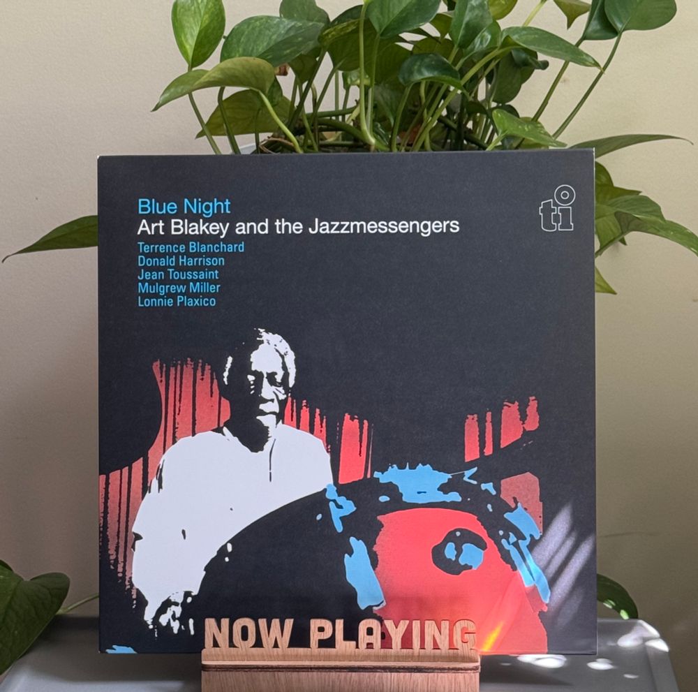 A record album in a stand on a table with a plant behind it. 