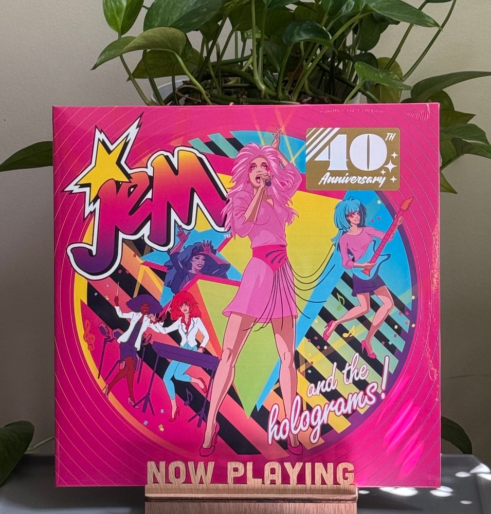A record album in a stand on a table with a plant behind it. 