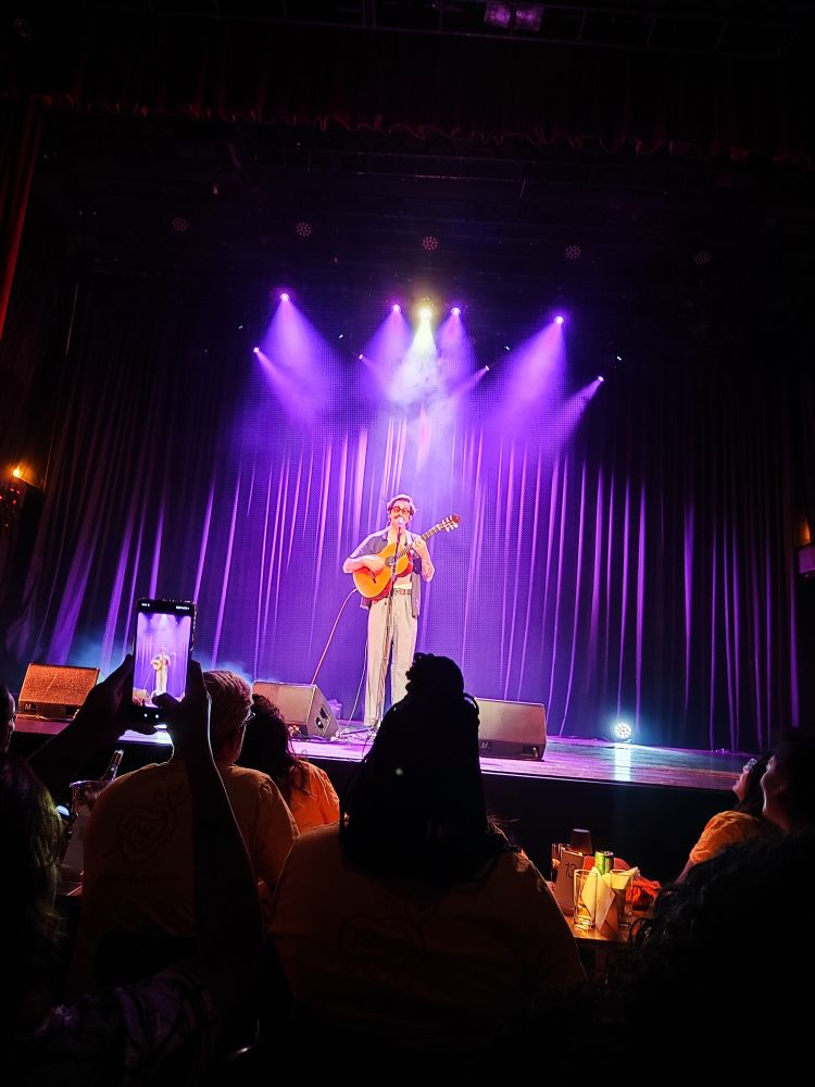 Foto do cantor Rodrigo Alarcon no palco tocando violão e cantando 
