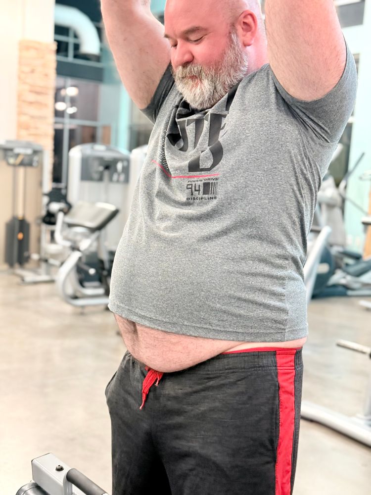 Big dad does a bicep pull down exercise while looking at his exposed underbelly 
