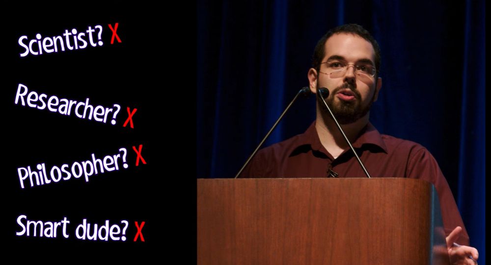 On the right-hand side of the image is Eliezer Yudkowsky, a white man with short dark hair and full facial hair and glasses; on the left-hand side is written "Scientist? Researcher? Philosopher? Smart dude?" each with a question mark and a red X next to it.