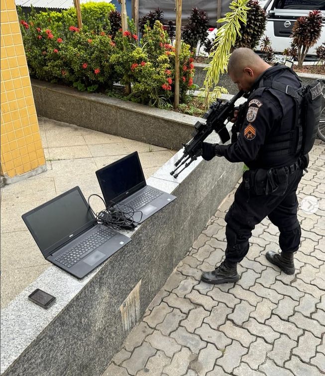 Police officer pointing his rifle at 2 computers. DrugBust