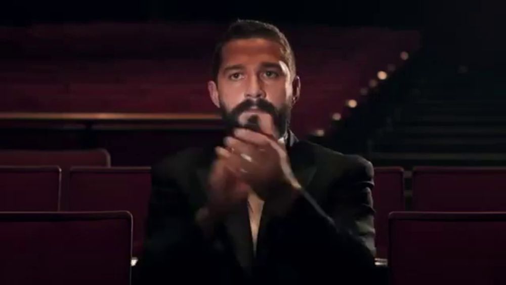 a man in a tuxedo and bow tie is sitting in a theater applauding .