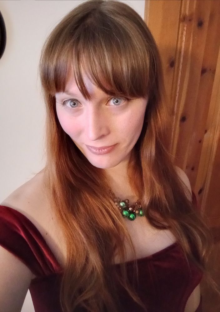 A photo of me, in red Christmas outfit, long reddish brown hair, blue eyes w/ yellow-rings,