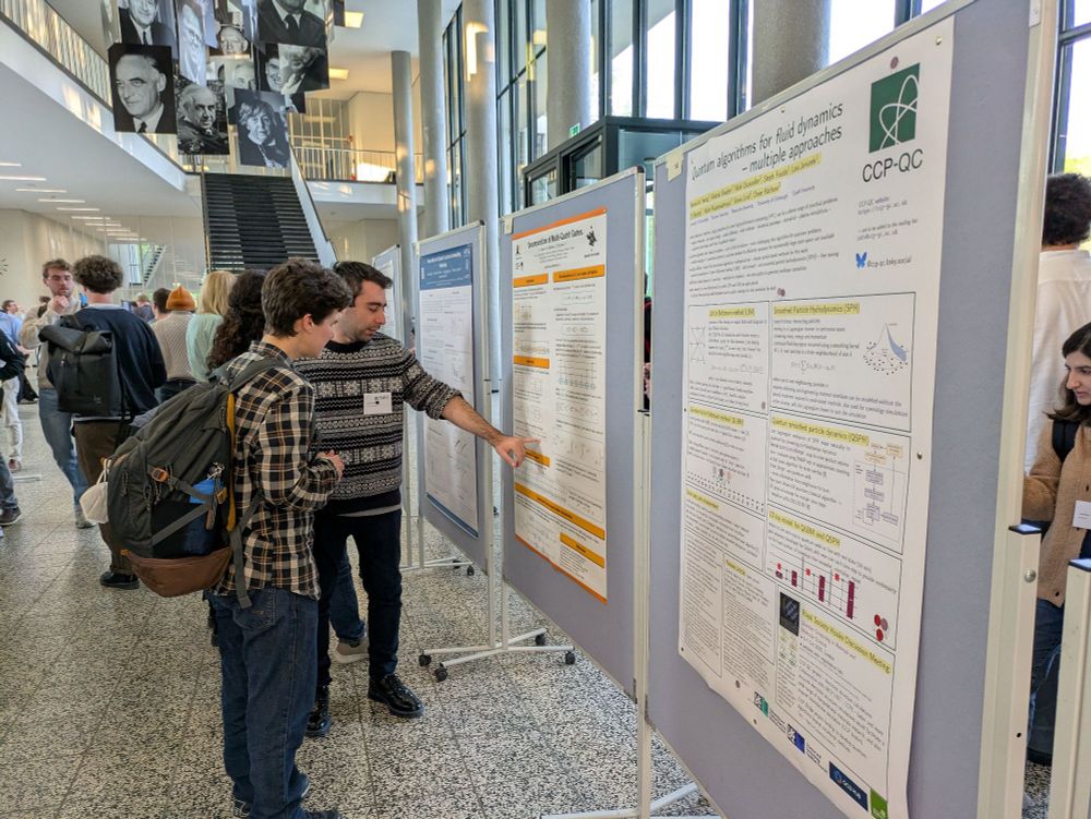 Row of poster boards stretching away in centre with two people in foreground discussing second poster in row. Portraits of academics hanging from wires above
