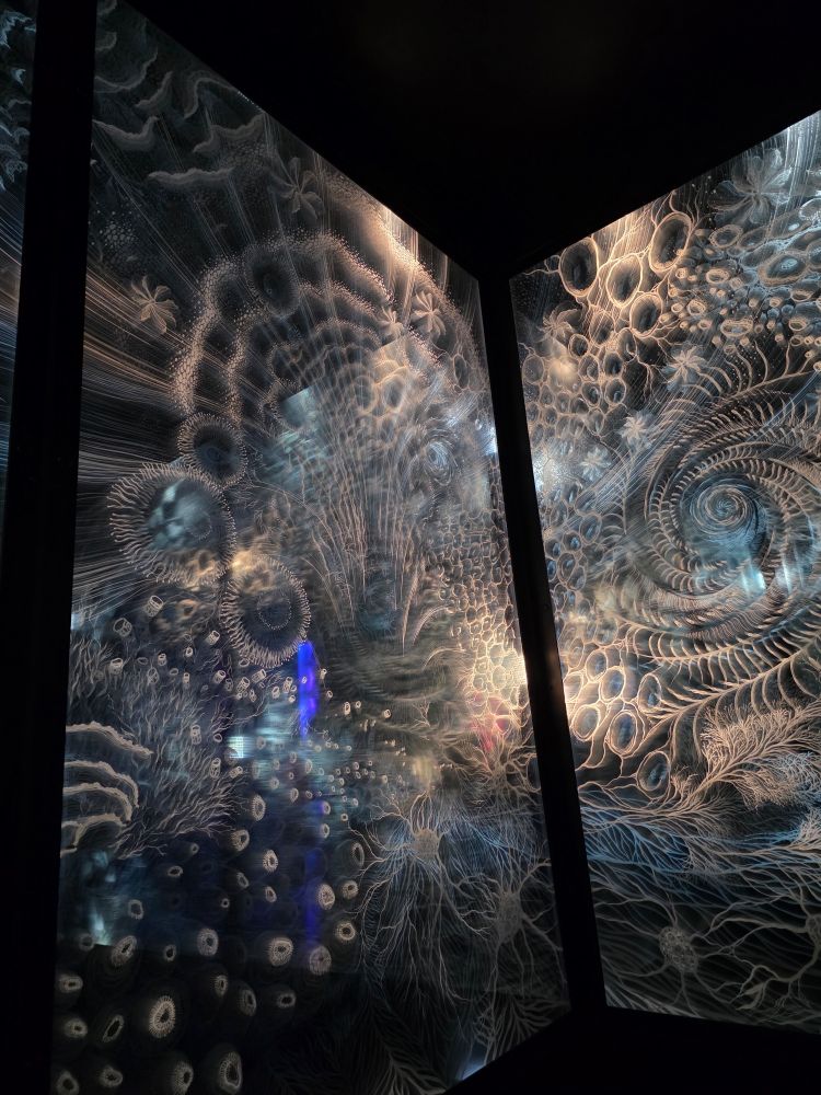 Horizontal stacked glass panels with etchings that represent spirals and neurons. Light is also projected from the side to make it seem like it's moving