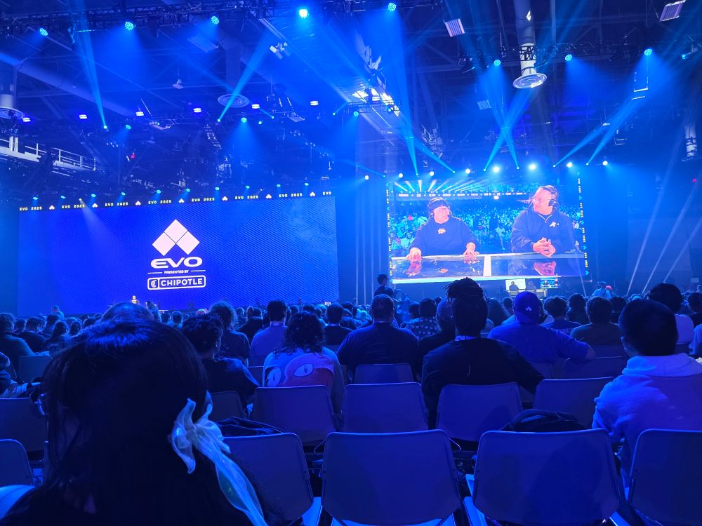 EVO arena that has Justin Wong and yipes on the big screen. It's a floor view of the big screens bathed in blue lighting 