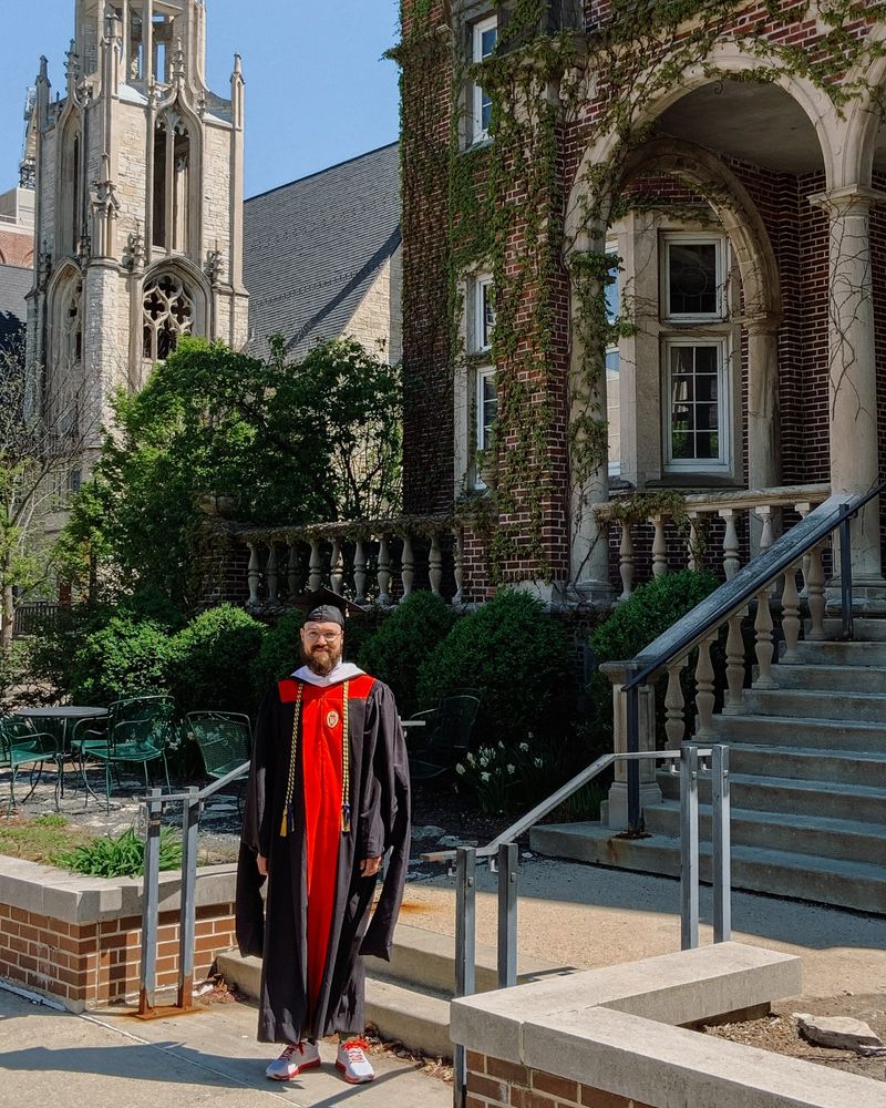 Forrest Ashworth stands in front of University Club Building in cap and gown. 