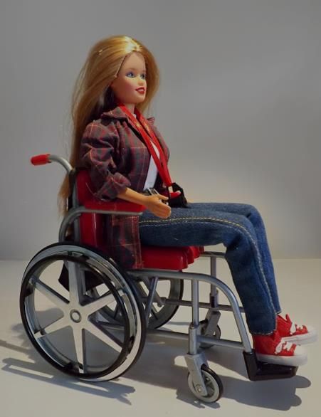 Eine Barbie, die einen Rollstuhl sitzt und Fotografin ist.