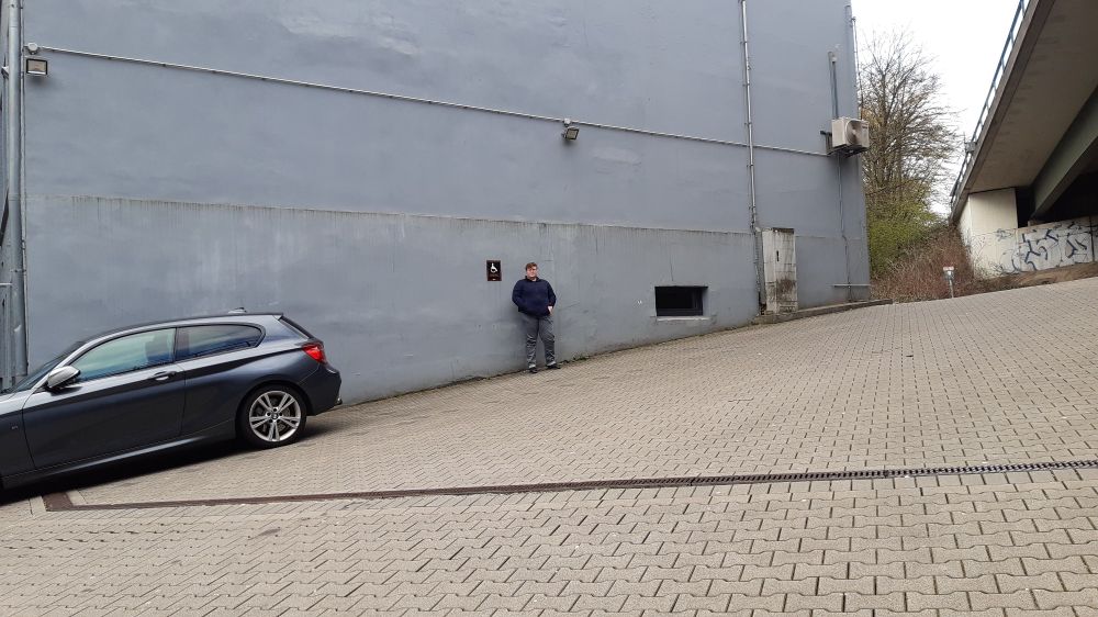 Hier dasselbe Bild im Weitwinkel aufgenommen. Erst jetzt sieht man wie heftig die Steigung wirklich ist. Unrealistisch, dass dort ein Rollstuhlnutzender wirklich parken bzw. aus- oder einsteigen kann.