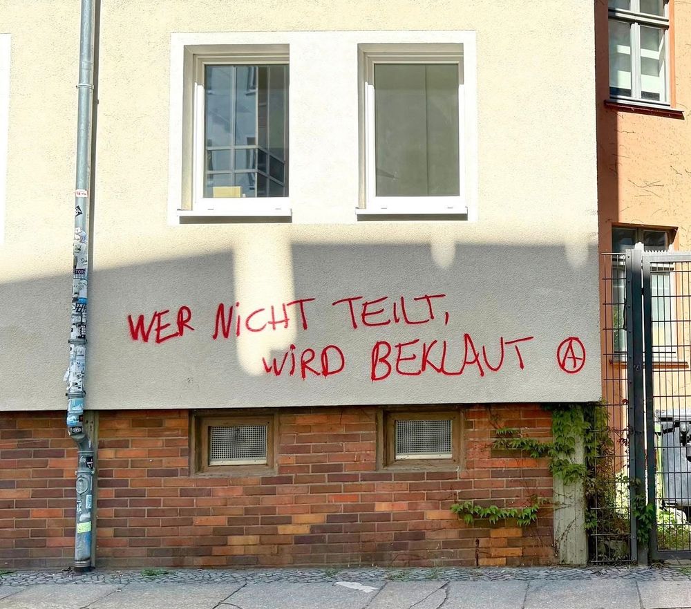Graffiti an Hauswand: Wer nicht teilt, wird beklaut. Dazu ein A im Kreis.