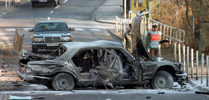 Foto vom Tatort. Das schwer beschädigte Auto Herrhausen steht quer auf der Fahrbahn,  Polizisten untersuchen das Wrack.