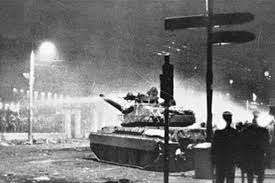 Bei Nacht aufgenommene Schwarz-Weiß-Fotografie, im Vordergrund ein Panzer, dessen Kanone in Richtung des Athener Universitätstors zeigt.