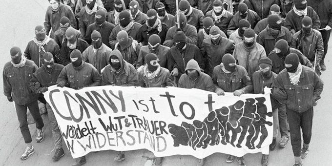 Schwarz-Weiß-Fotografie der Demonstration in Gedenken an Conny, einige Dutzend vermummte Antifaschisten, die erste Reihe trägt ein Transparent mit der Aufschrift "Conny ist tot - wandelt Wut und Trauer in Widerstand".