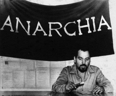 Foto von Pinelli vor einer schwarzen Fahne mit dem Aufdruck "Anarchia".
