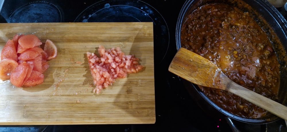 Bolognese köchelt vor sich hin, daneben ein Brett mit zur Hälfte gehackten Tomaten. 