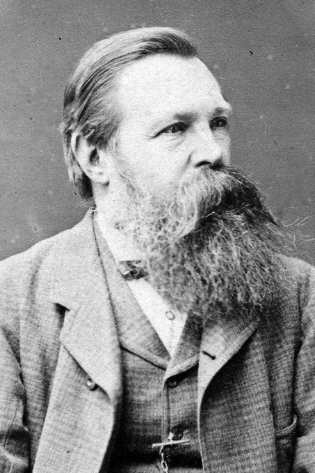 Portrait von Engels. Zum karierten Anzug hat er die Haare nach hinten gekämmt, er trägt einen enormen Schnauz- und wilden Vollbart.