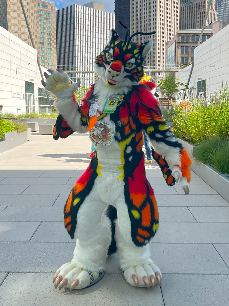 Enzo, the monarch butterfly tiger, standing on the rooftop garden of the D.L. Lawrence Convention Center during Anthrocon 2024, Pittsburgh cityscape in the background