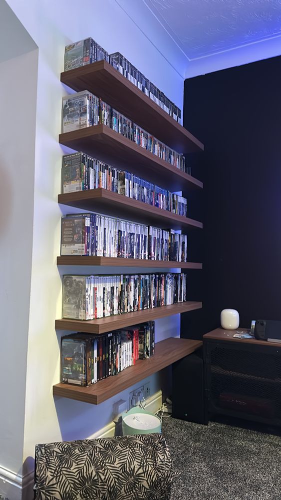Six walnut floating shelves supporting hundreds of games.