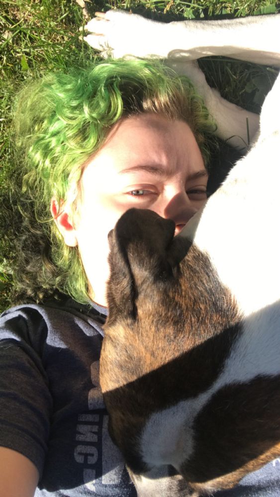irl Psuedo with green hair laying in the grass and a pit bull boxer mix dog (Nova) on top of them.