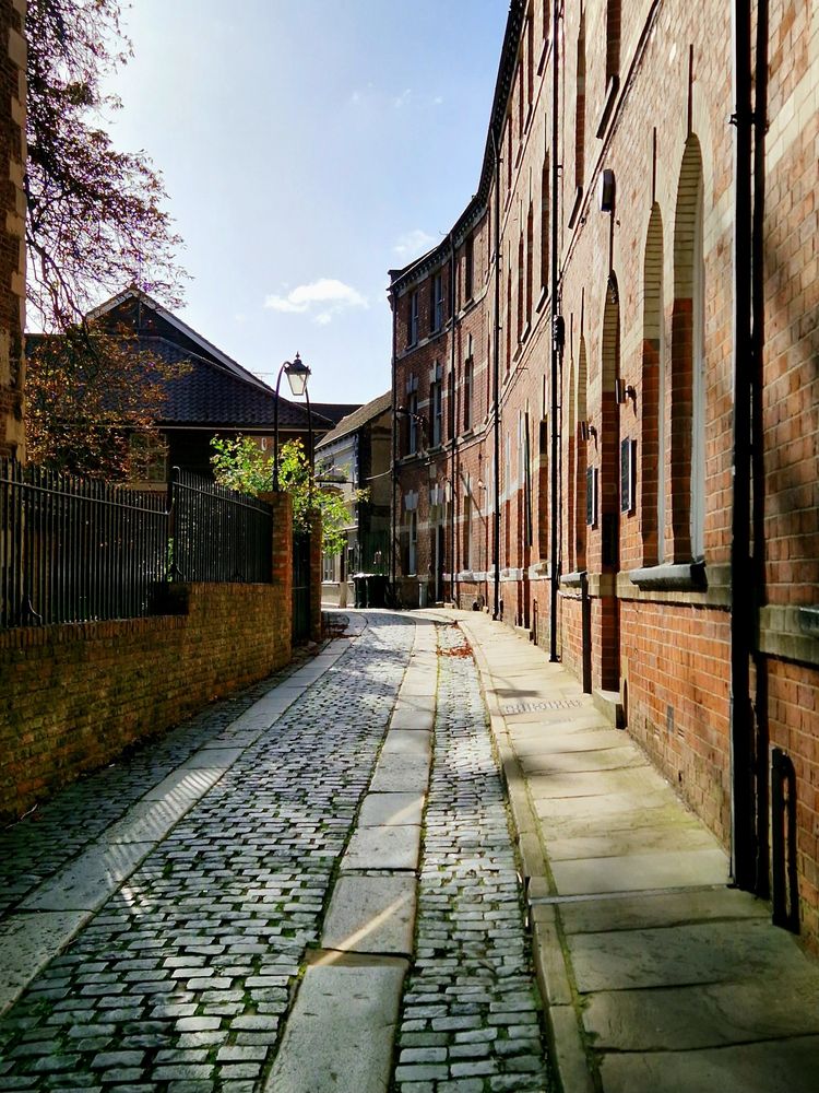 A narrow cobbled alleyway lined with brick buildings lit by the morning sun.