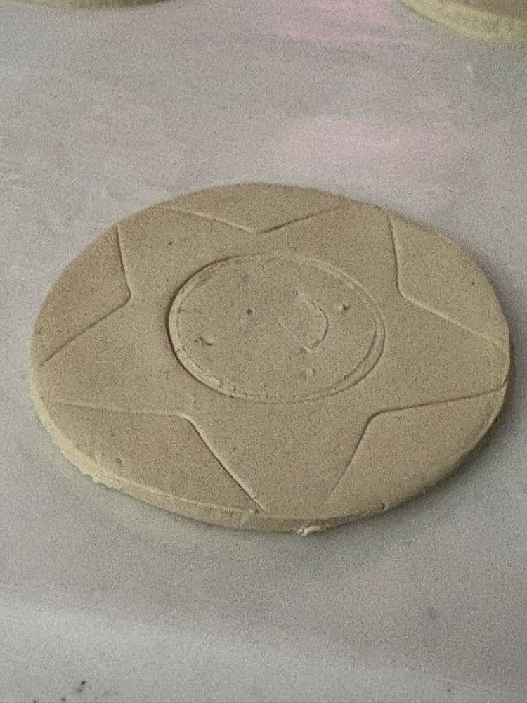 Thin clay circle with an indentation of a star inside.  Inside the star is a circle indentation meant for a tea light candle.