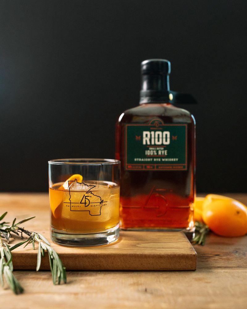 Ingredients:
- 2 oz. 45th Parallel R100 Rye Whiskey
- Barspoon of Demerara
- Barspoon of Honey Syrup
- 5 Dashes of Angostura Bitters
- 1 Sprig of Fresh Rosemary
- 1 Orange Twist for Garnish

Directions:

1. Gather a kitchen torch or lighter, a lowball glass, and a ceramic plate. Lay the rosemary sprig on the plate, lightly burn the rosemary, and set the lowball glass over it (upside down) to let smoke gather for at least ten seconds (leave longer for a more smokey effect). 

2. Once the glass is smoked to preference, remove from the rosemary. Place one large ice cube in the lowball, followed by all liquid ingredients, and stir gently until combined.

3. Express the orange zest over the glass as you create the twist, garnish the cocktail, and enjoy!