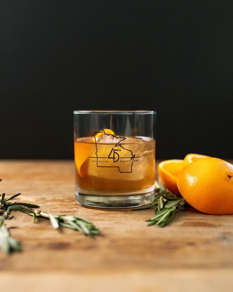 Ingredients:
- 2 oz. 45th Parallel R100 Rye Whiskey
- Barspoon of Demerara
- Barspoon of Honey Syrup
- 5 Dashes of Angostura Bitters
- 1 Sprig of Fresh Rosemary
- 1 Orange Twist for Garnish

Directions:

1. Gather a kitchen torch or lighter, a lowball glass, and a ceramic plate. Lay the rosemary sprig on the plate, lightly burn the rosemary, and set the lowball glass over it (upside down) to let smoke gather for at least ten seconds (leave longer for a more smokey effect). 

2. Once the glass is smoked to preference, remove from the rosemary. Place one large ice cube in the lowball, followed by all liquid ingredients, and stir gently until combined.

3. Express the orange zest over the glass as you create the twist, garnish the cocktail, and enjoy!