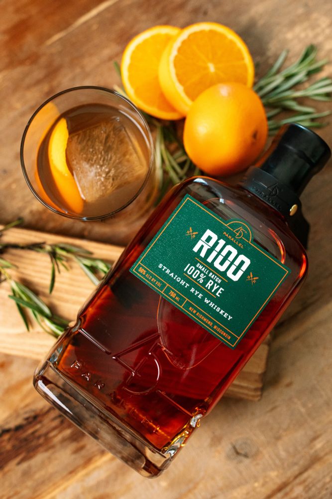 Ingredients:
- 2 oz. 45th Parallel R100 Rye Whiskey
- Barspoon of Demerara
- Barspoon of Honey Syrup
- 5 Dashes of Angostura Bitters
- 1 Sprig of Fresh Rosemary
- 1 Orange Twist for Garnish

Directions:

1. Gather a kitchen torch or lighter, a lowball glass, and a ceramic plate. Lay the rosemary sprig on the plate, lightly burn the rosemary, and set the lowball glass over it (upside down) to let smoke gather for at least ten seconds (leave longer for a more smokey effect). 

2. Once the glass is smoked to preference, remove from the rosemary. Place one large ice cube in the lowball, followed by all liquid ingredients, and stir gently until combined.

3. Express the orange zest over the glass as you create the twist, garnish the cocktail, and enjoy!