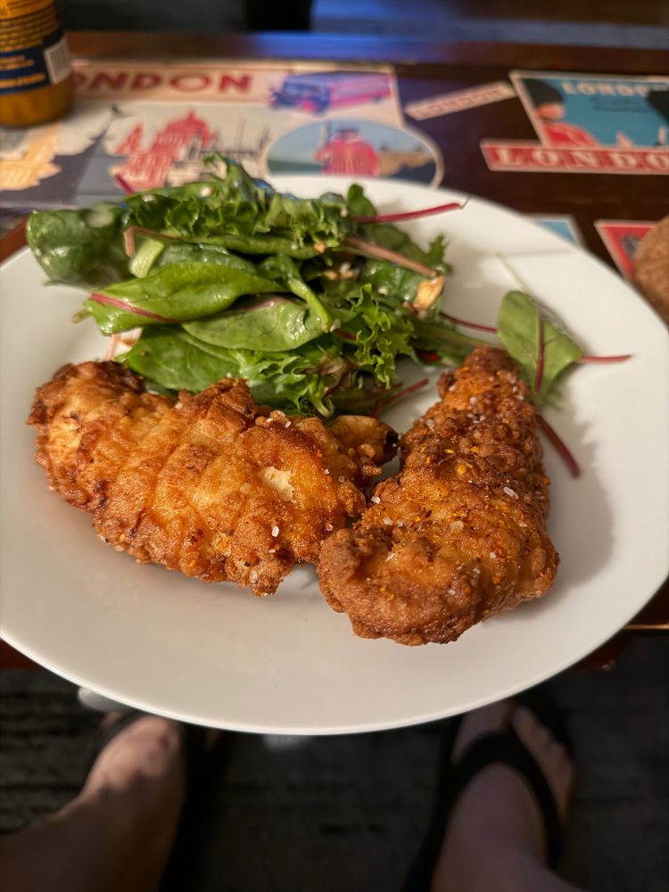 A plate with two golden fried chicken fingers and a Trader Joe’s harvest apple salad.