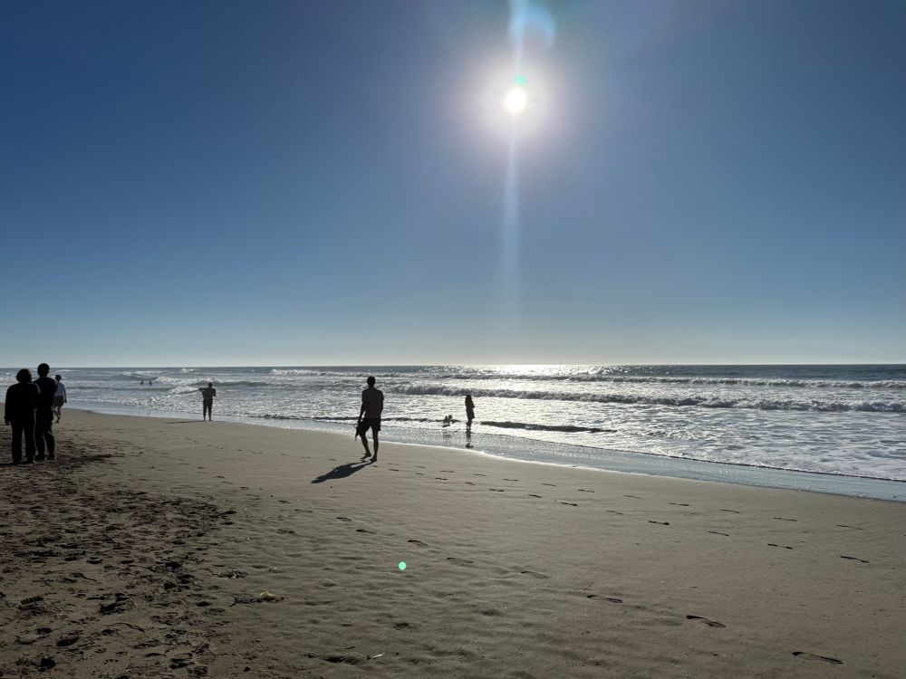 A shoreline with beach walkers on a clear blue sunny afternoon 
